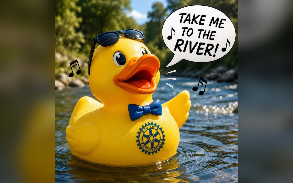 A yellow rubber duck wearing sunglasses and a Rotary bow tie, floating on the river, saying take me to the river.